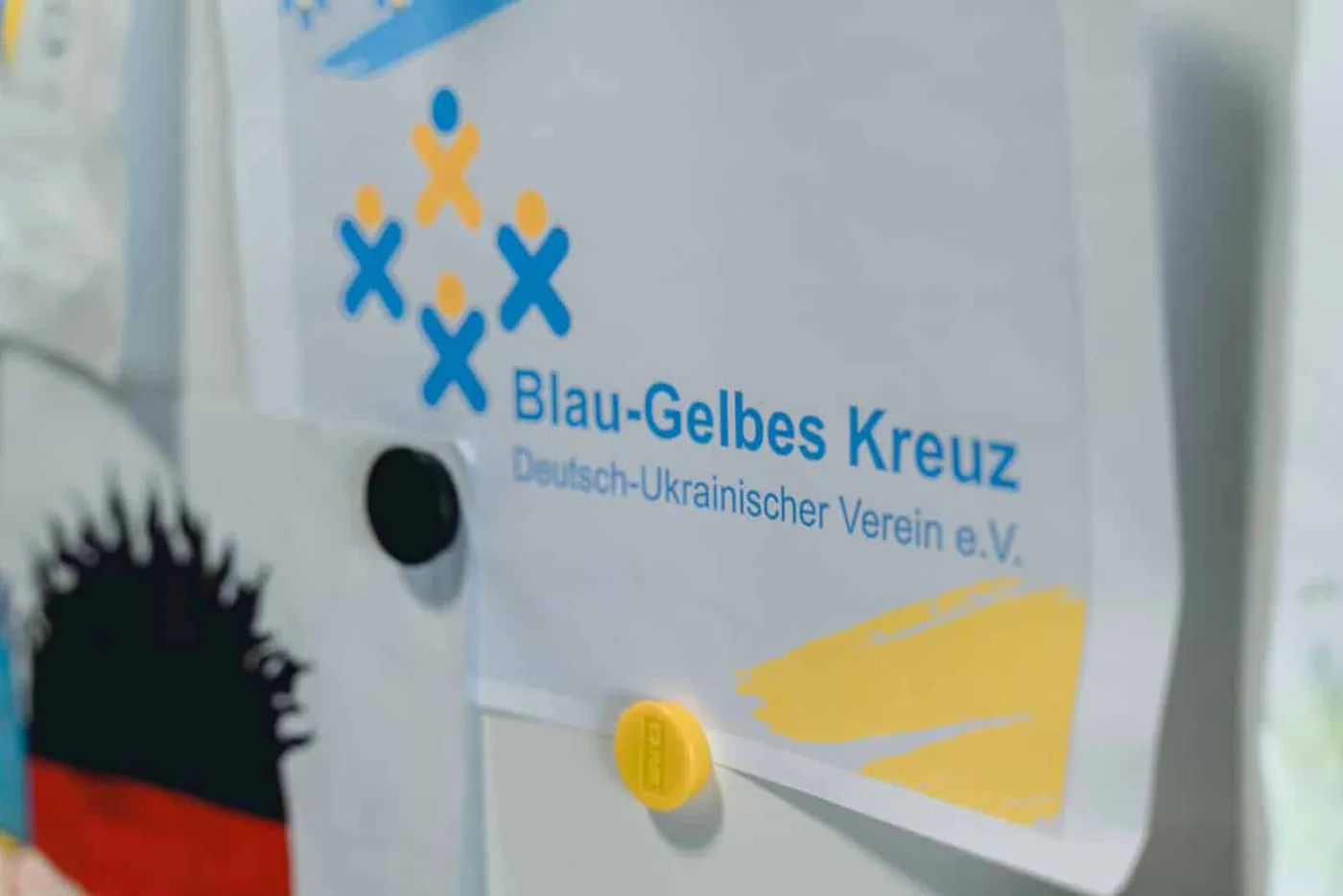 Aushang mit Logo und Schriftzug „Blau-Gelbes Kreuz – Deutsch-Ukrainischer Verein e.V.“ an einer Pinnwand.