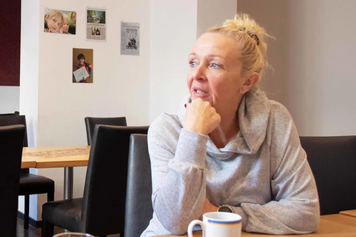 Eine Frau im grauen Sweatshirt sitzt am Tisch.