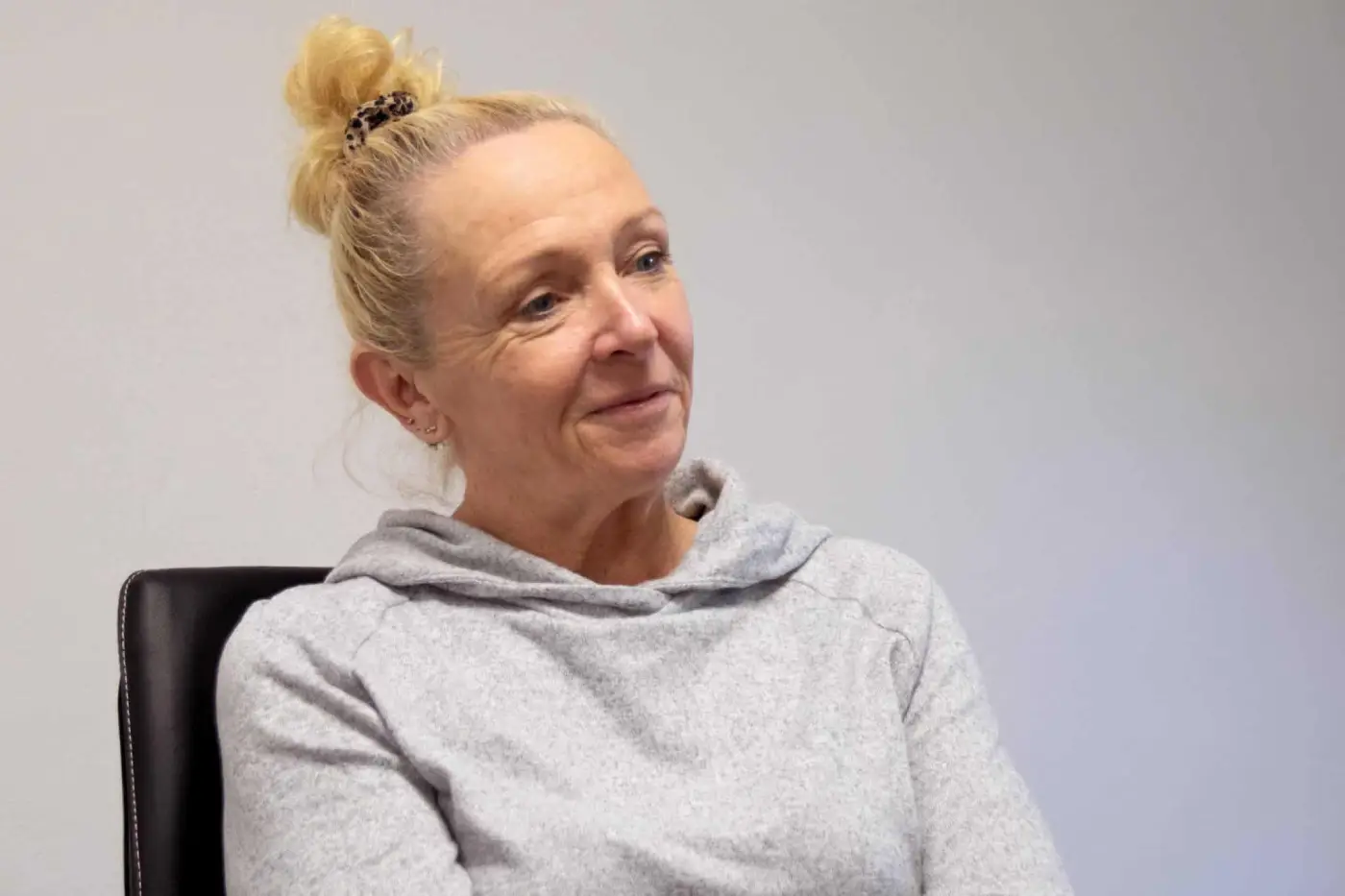 Eine Frau im grauen Sweatshirt sitzt auf einem Stuhl.