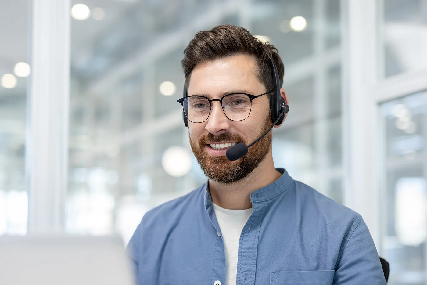 Mann mit Headset und Brille lächelt während eines Meetings in seine Kamera.