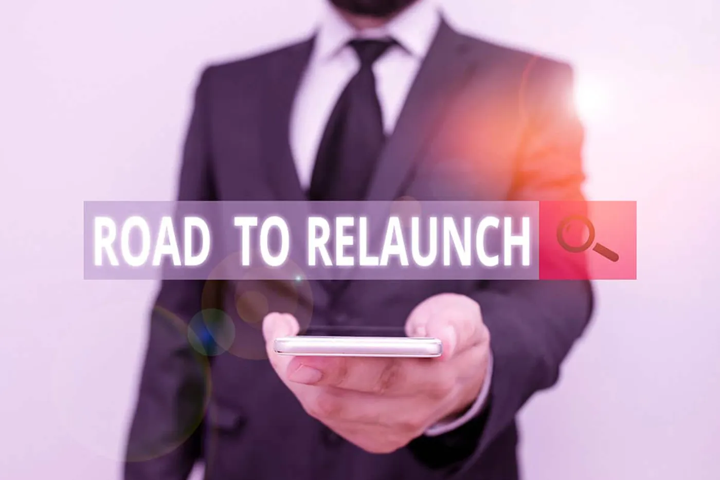 Herr im Anzug hält ein Smartphone nach vorne, darüber eingeblendeter Schriftzug „Road to Relaunch“ mit Lupensymbol.