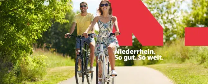 Zwei Radfahrer fahren in der Sonne mit ihrem Fahrrad durch ein Waldstück.