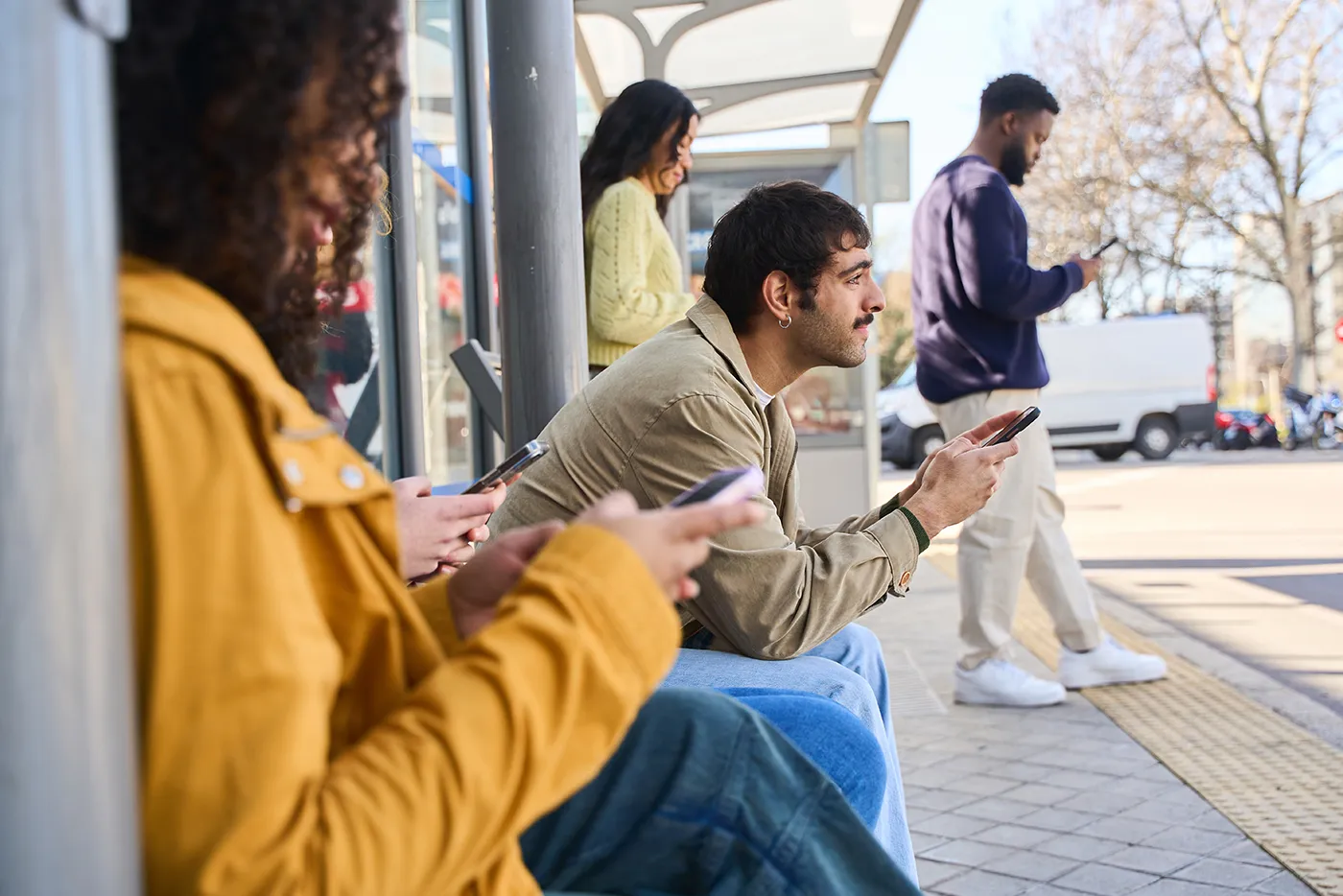Mehrere Menschen warten an einer Bushaltestelle und nutzen ihre Smartphones. Das Bild veranschaulicht die alltägliche Nutzung digitaler Medien.