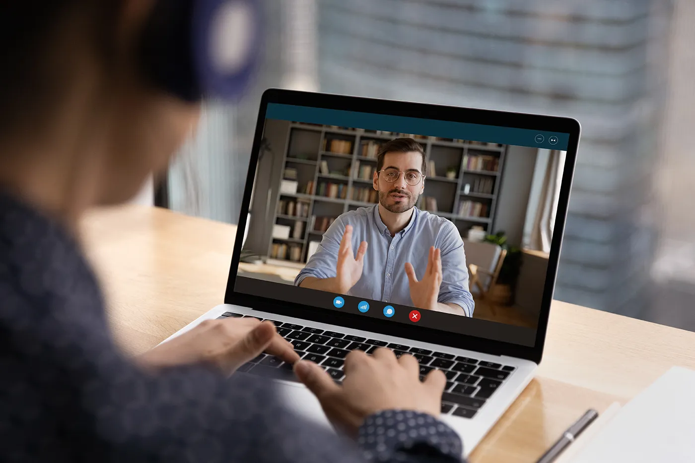 Person sitzt an einem Laptop und führt ein Videointerview mit einem Mann, der auf dem Bildschirm zu sehen ist und während des Gesprächs gestikuliert.